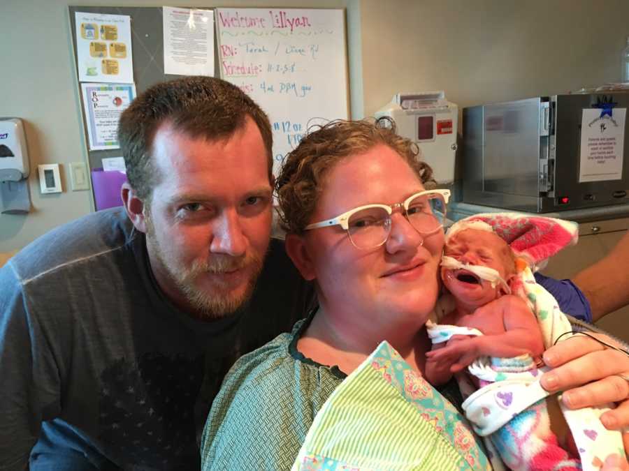 Husband smiles beside wife who holds crying newborn in NICU