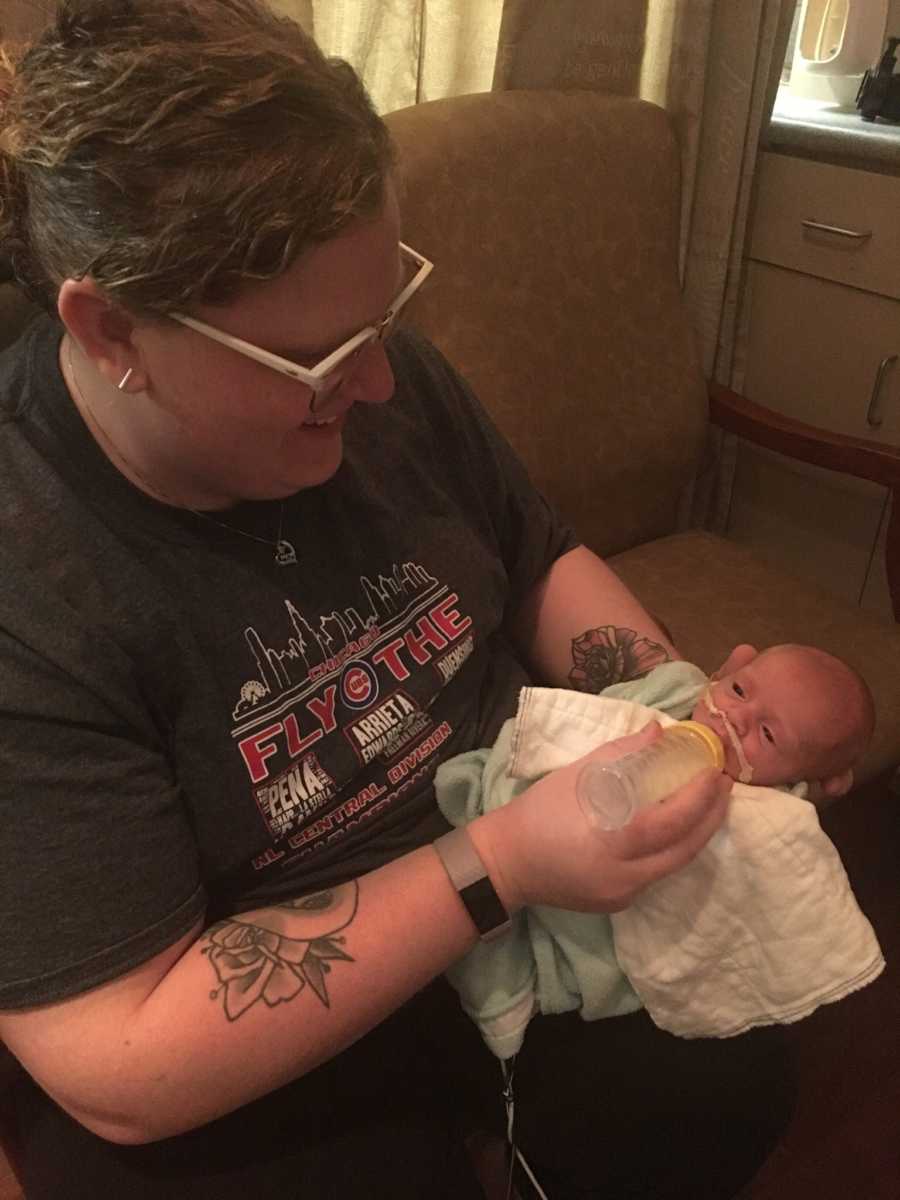Mother smiles as she sits feeding newborn in her arm with bottle