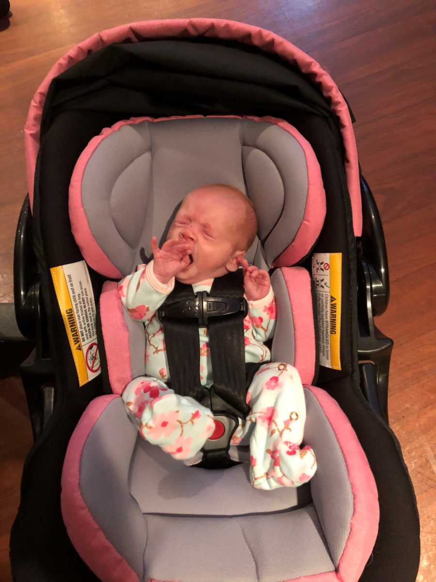 Newborn yawns as she sits in car seat