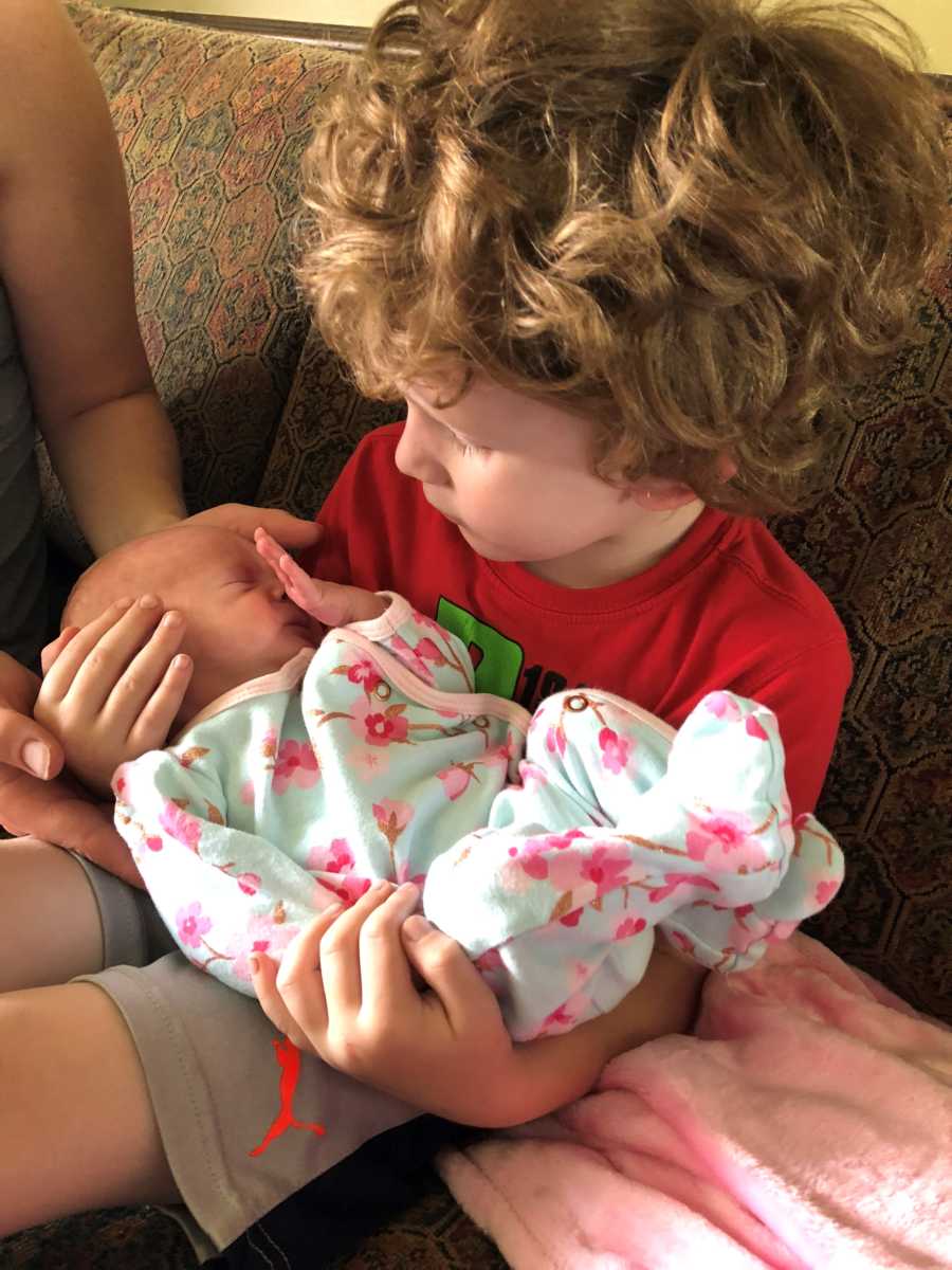 Little boy sits on couch holding baby sister in his lap