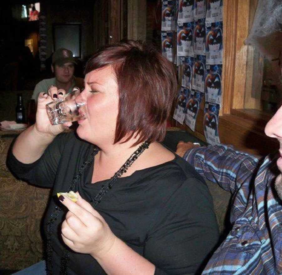 Alcoholic woman sits in booth of bar taking shot