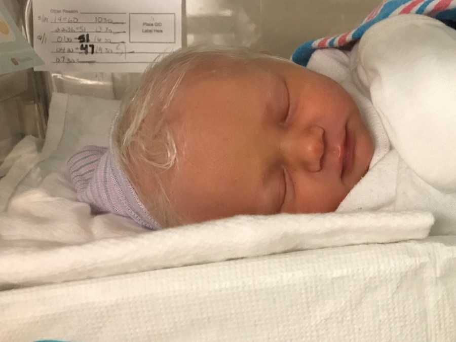 Newborn baby with bright white hair lays asleep in hospital