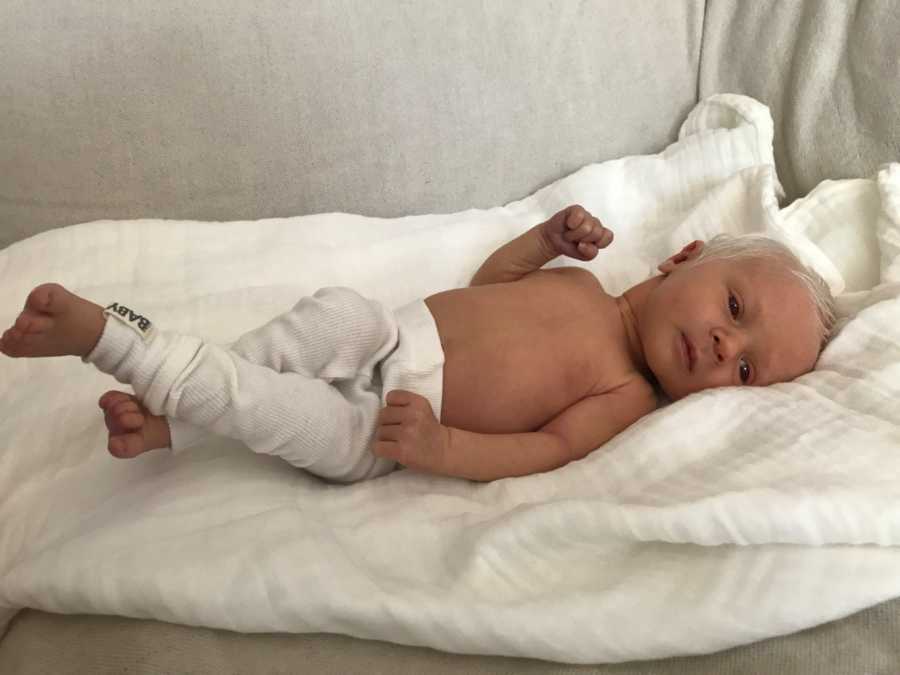 Albino baby lays on back on white blanket