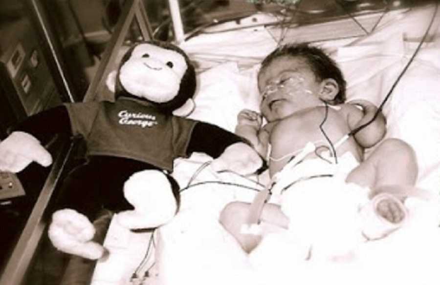 Preemie lays in NICU with Curious George stuffed animal laying beside him