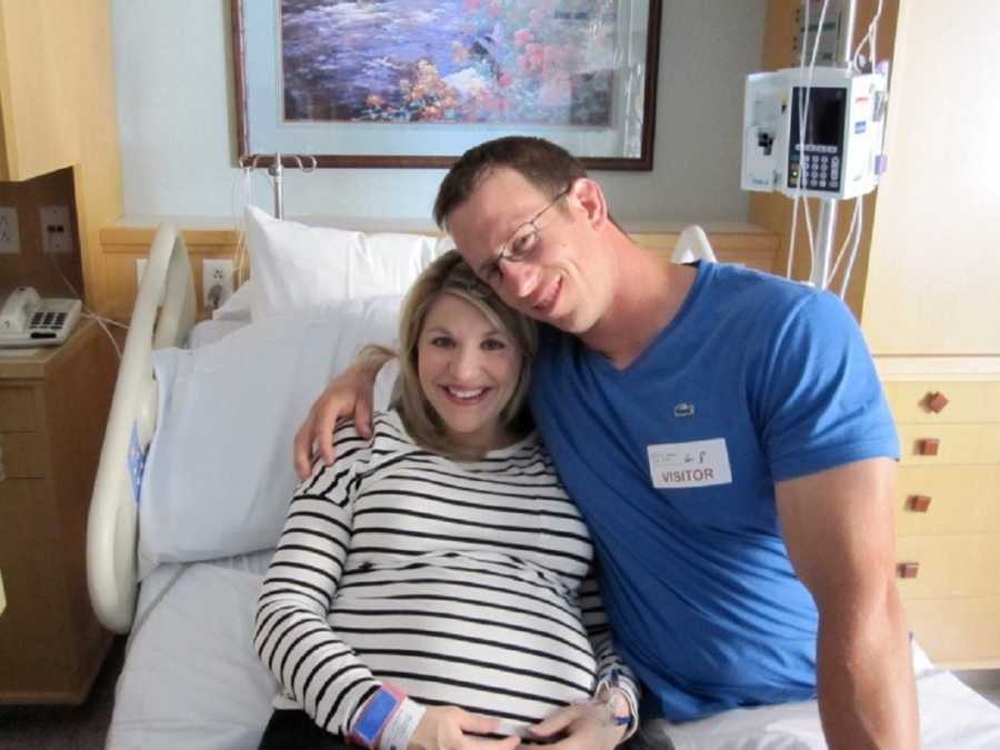 Pregnant woman lays in hospital bed as her husband sits smiling beside her