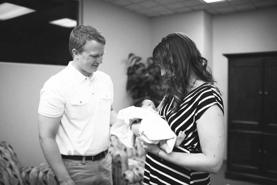 Husband smiles beside wife who holds their adopted newborn