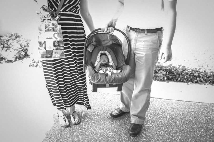Husband and wife stand holding carseat where there adopted baby sleeps