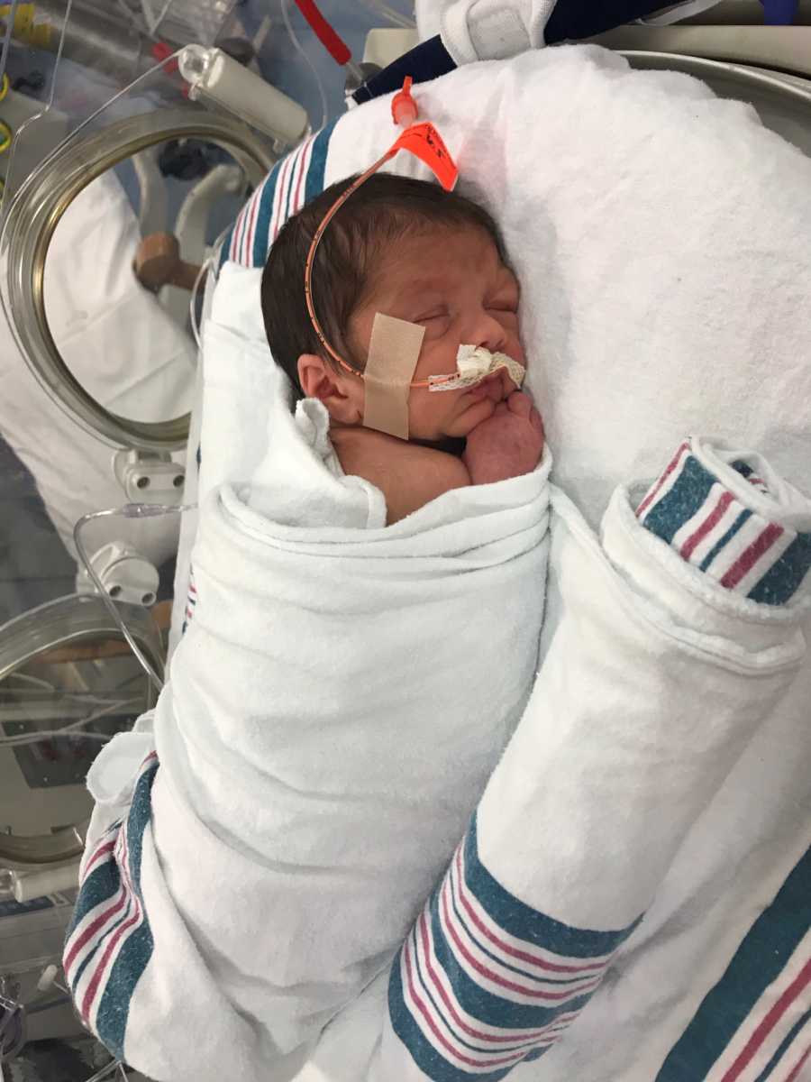 Newborn lays on stomach in NICU swaddled in blanket