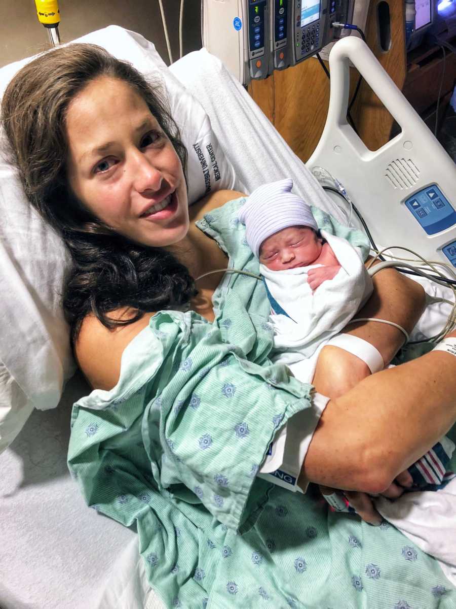 Mother smiles in hospital bed as she holds newborn in her arms