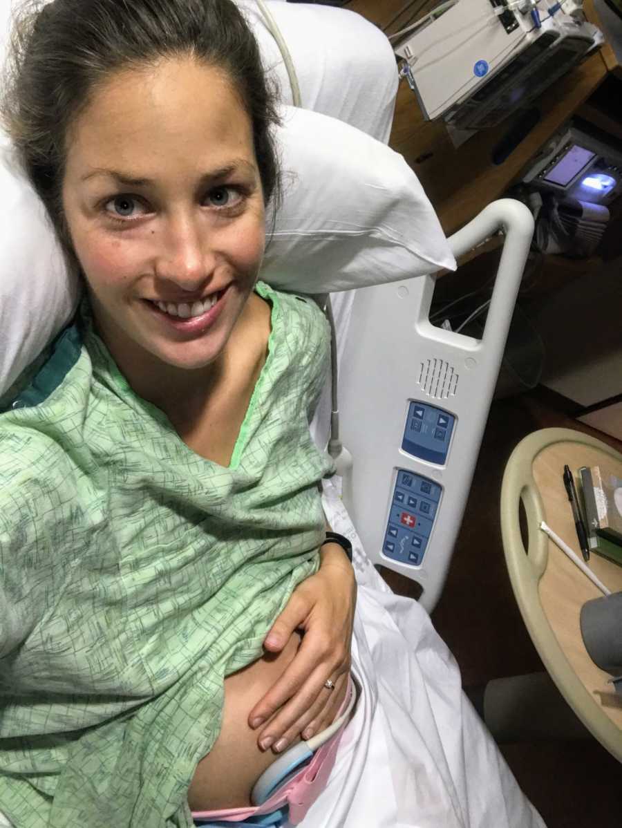 Pregnant active duty woman smiles in selfie as she lays in hospital bed holding stomach 