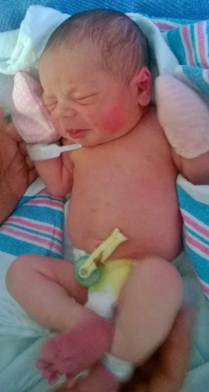 Newborn baby lays on back with pink mittens on