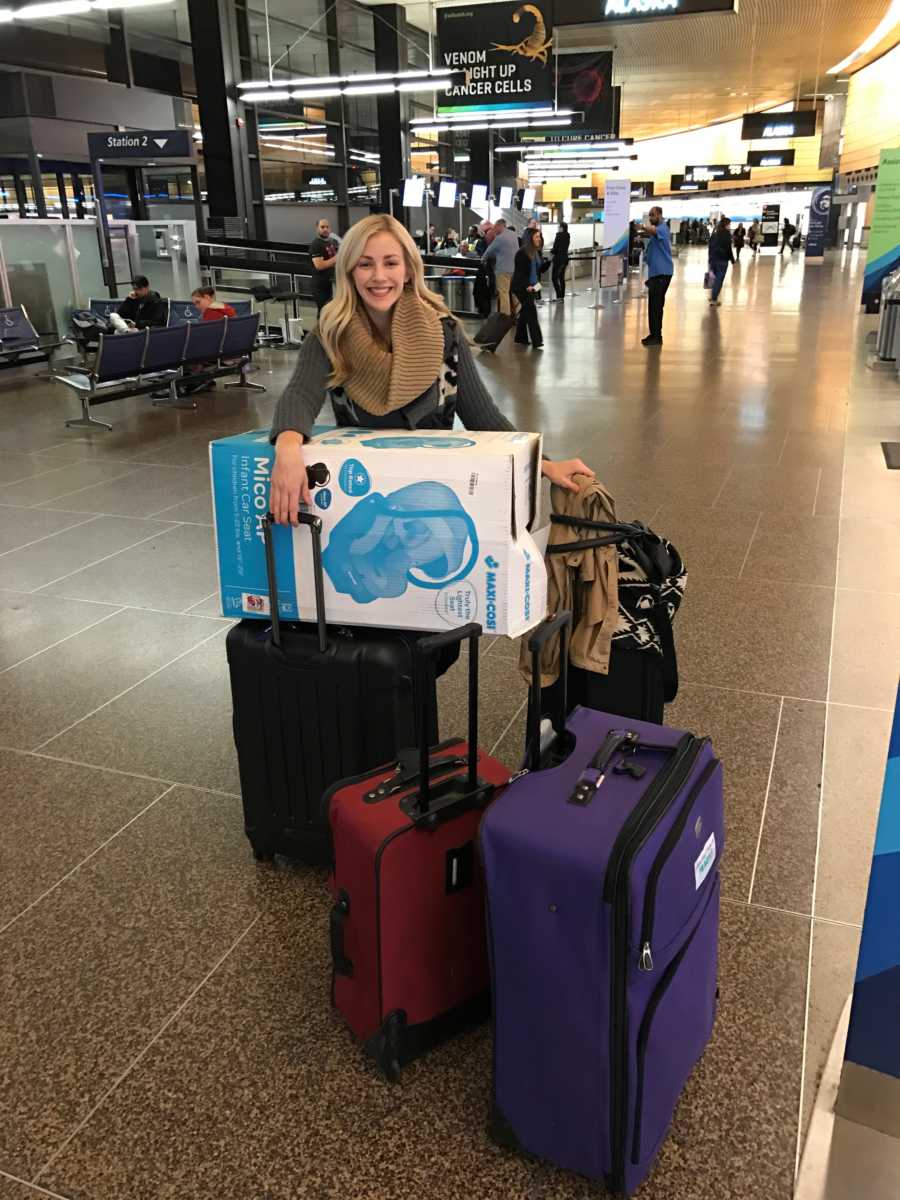 Woman stands in airport with four suitcases and box for new carseat