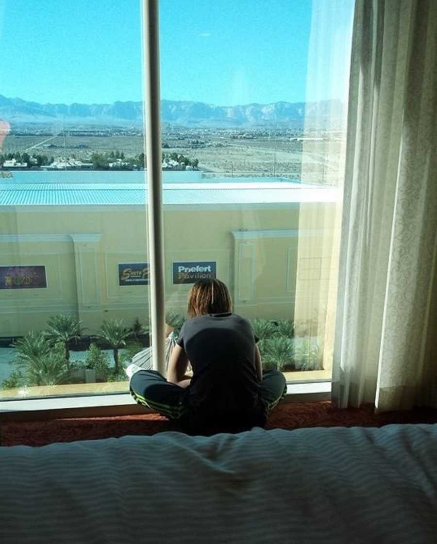 Young girl sitting on floor of hotel room looking out window