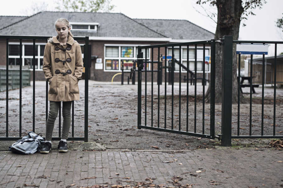 Young girl who wants a cell phone stands beside fence at school