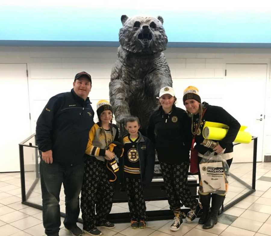 Husband and ex-wife stand with their two daughters and son in Boston Bruin clothes in front of bear statue