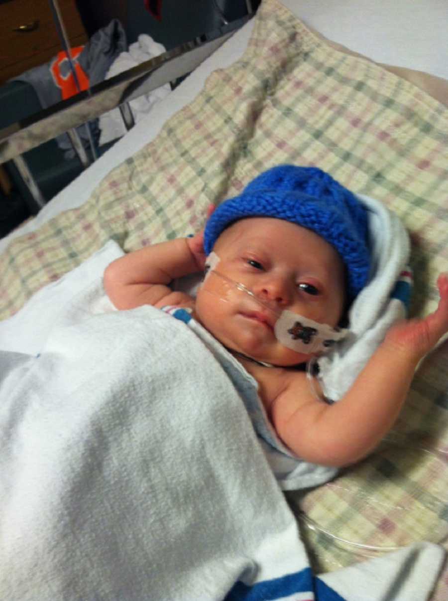 Baby with down syndrome and RSV lays in hospital with blue hat and tube up his nose