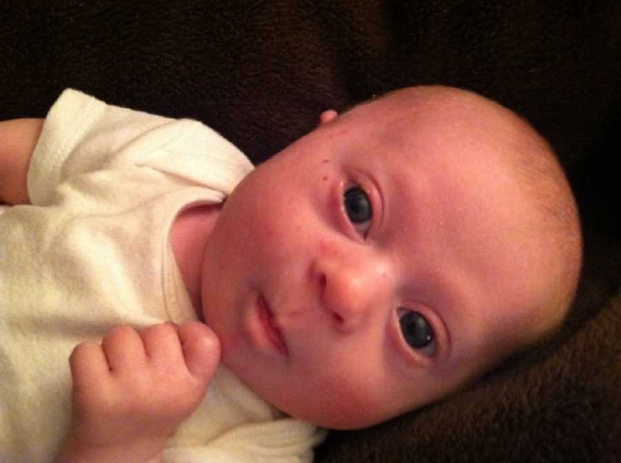 Baby boy with down syndrome lays on back wearing white onesie