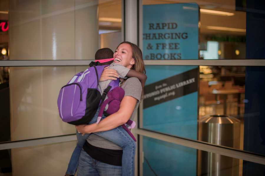 Mother smiles as she holds adopted daughter in her arms at airport