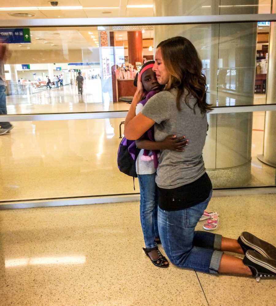 Mother kneels at airport crying as she hugs adopted daughter