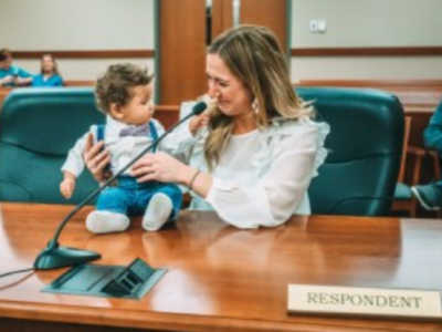 Woman sits at desk at adoption court smiling as she looks at little boy who sits on desk
