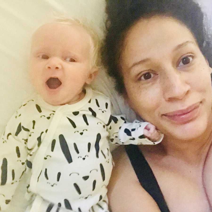Mother lays on back smiling in selfie beside albino baby