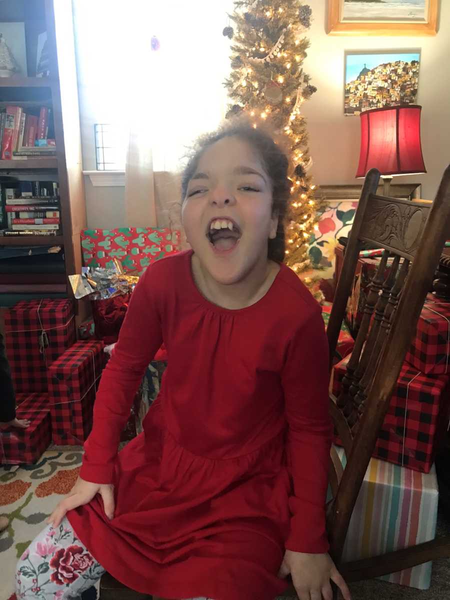 Young girl with special needs sits in chair in foster home with Christmas tree and presents in background