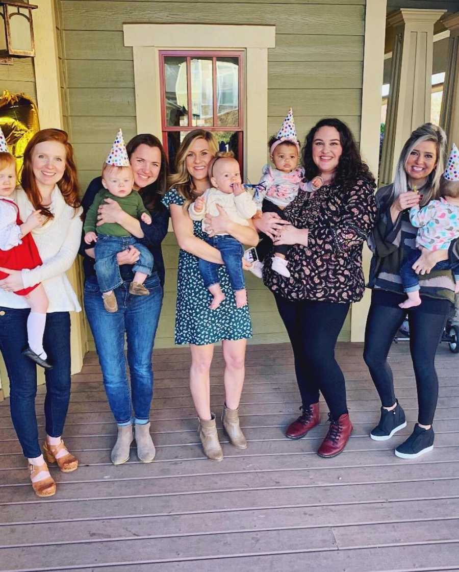 Five woman stand outside a home holding their babies