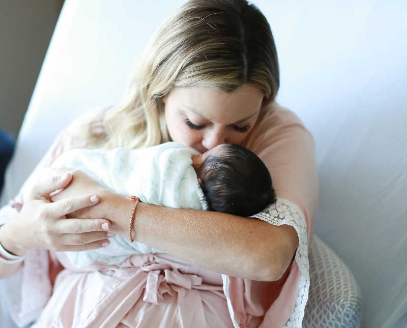 Woman kisses newborn who she holds in her arms in hospital bed