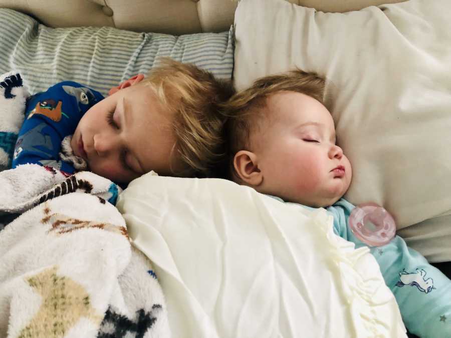 Little boy lays in bed asleep with baby sister