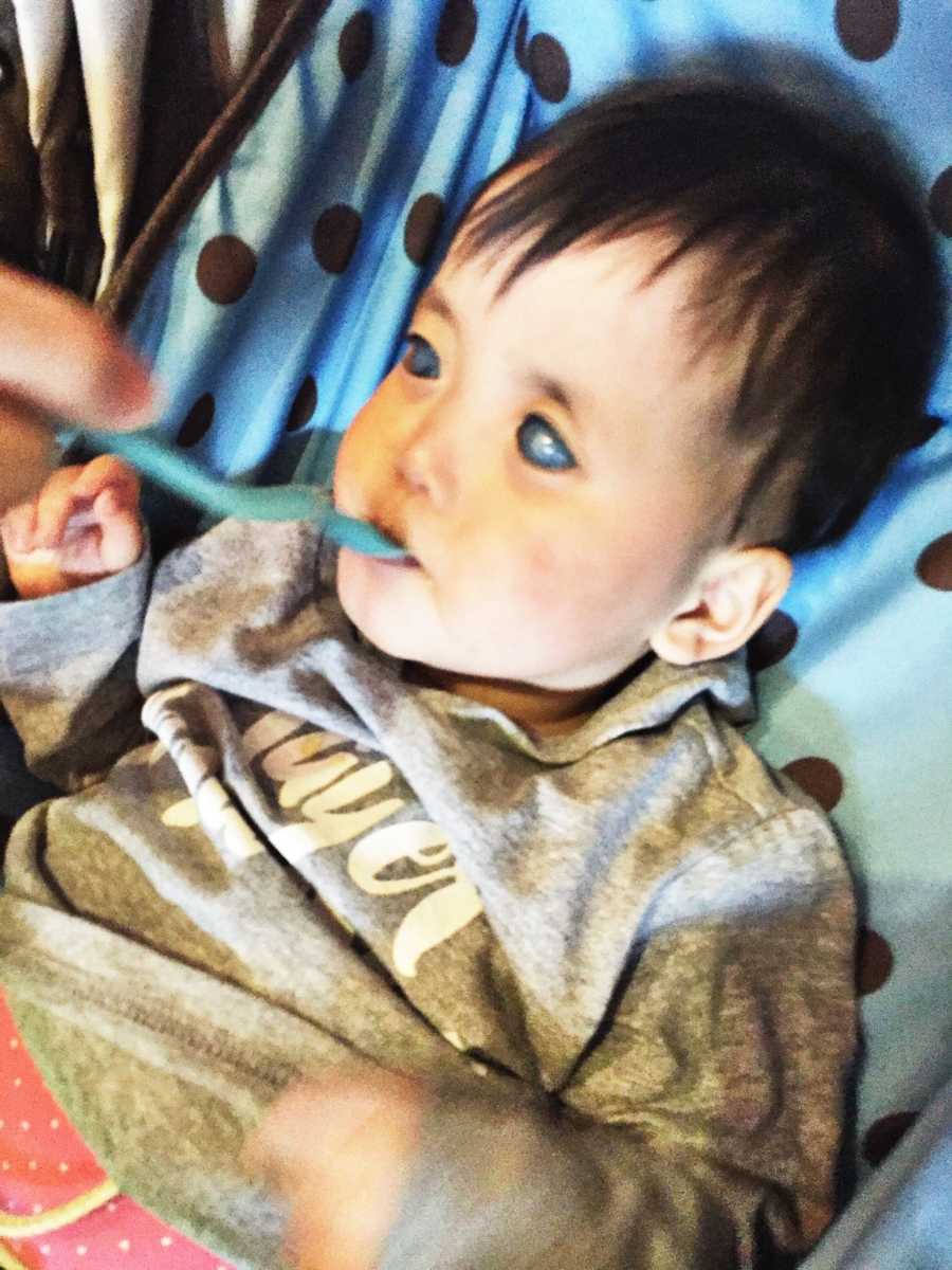 Blind and deaf baby lays on back as someone feeds her spoonful of food