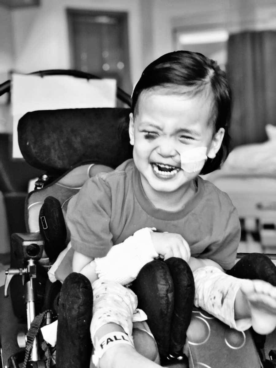 Blind and deaf little girls sits in wheelchair laughing with tube up her nose