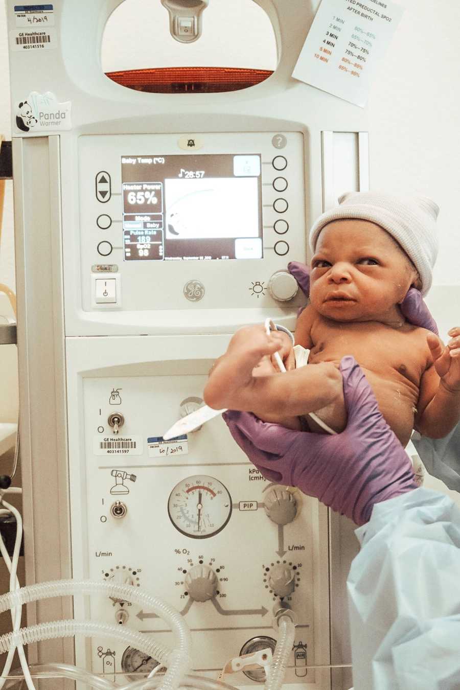 Newborn is held by doctor in front of monitor