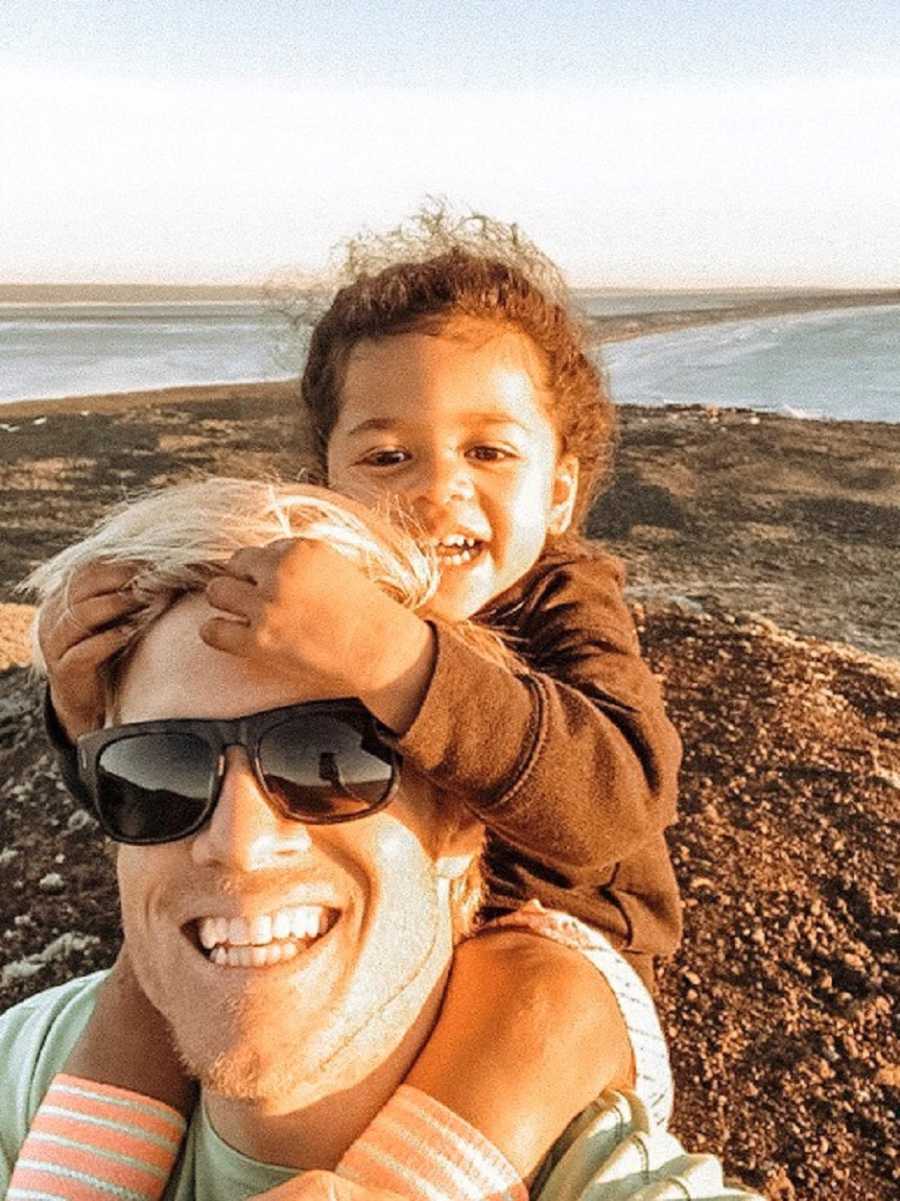 Father smiles in selfie with adopted daughter sitting on his shoulders