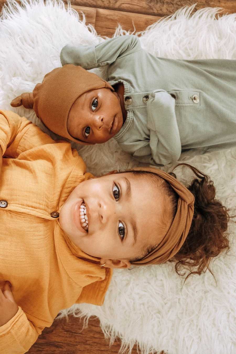 Adopted little girl lays smiling on her back with adopted baby brother beside her