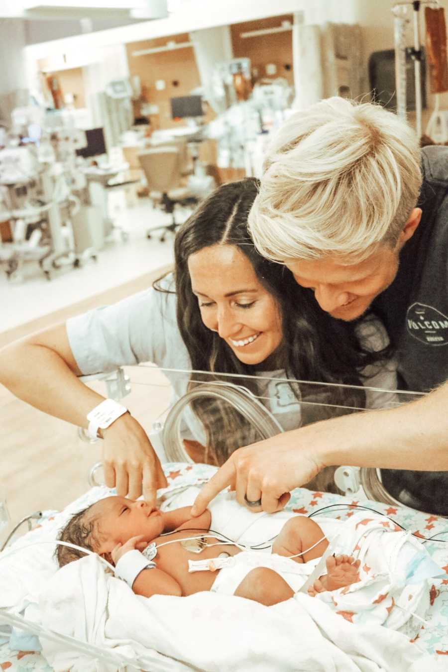 Husband and wife stands smiling over newborn they are adopting