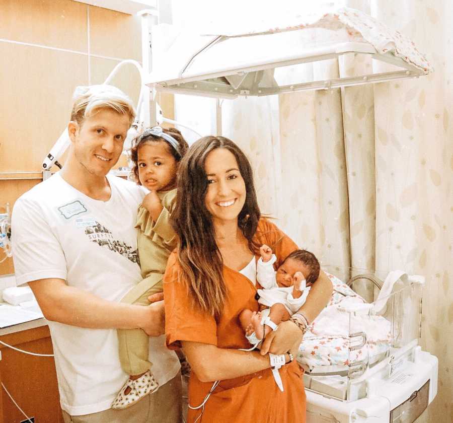 Husband and wife stand in hospital room with their two adopted children