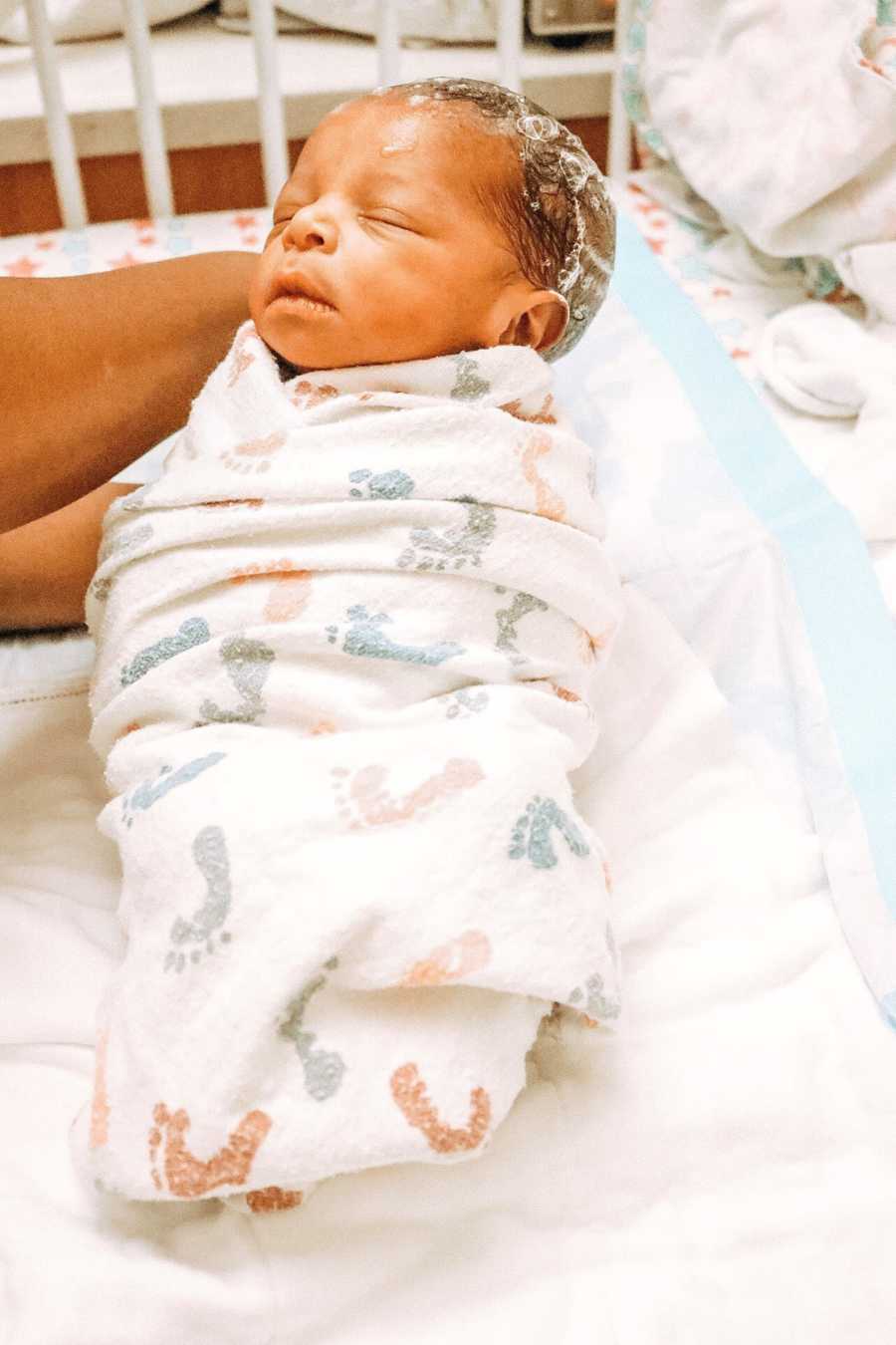 Newborn with soap suds on her head lays asleep in hospital blanket