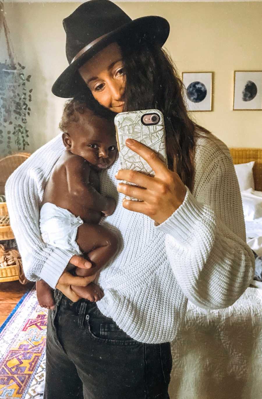 Mother smiles in mirror selfie while holding adopted baby
