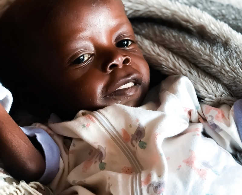 SIck Kenyan orphan lays on her back smiling