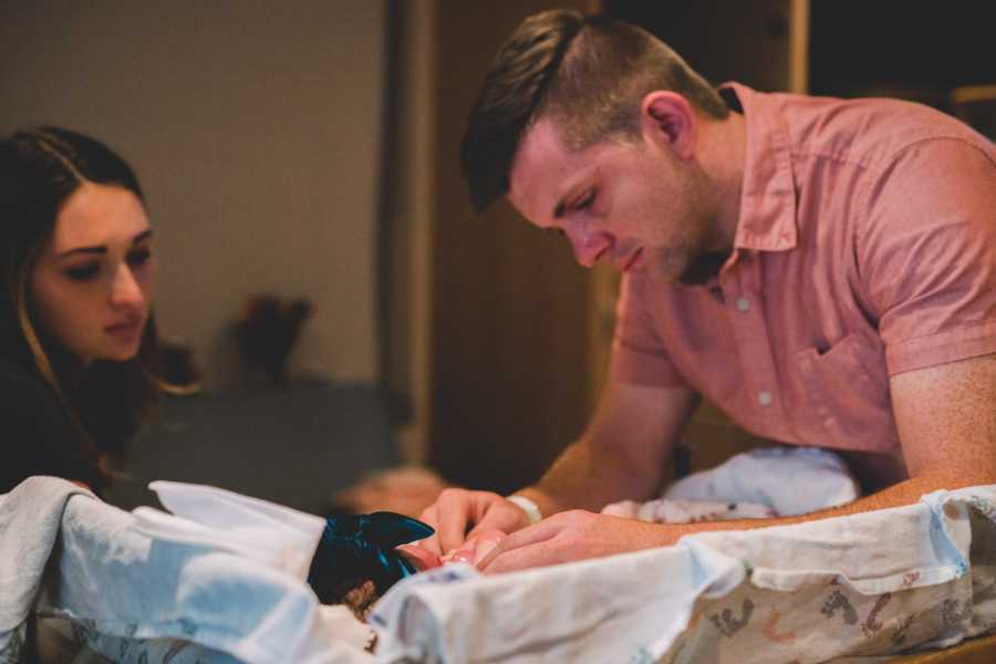 Father cries as he stands over newborn lying on her back