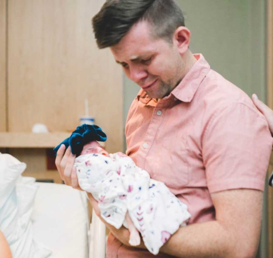 Father cries as he holds newborn daughter swaddled in blanket in his arms