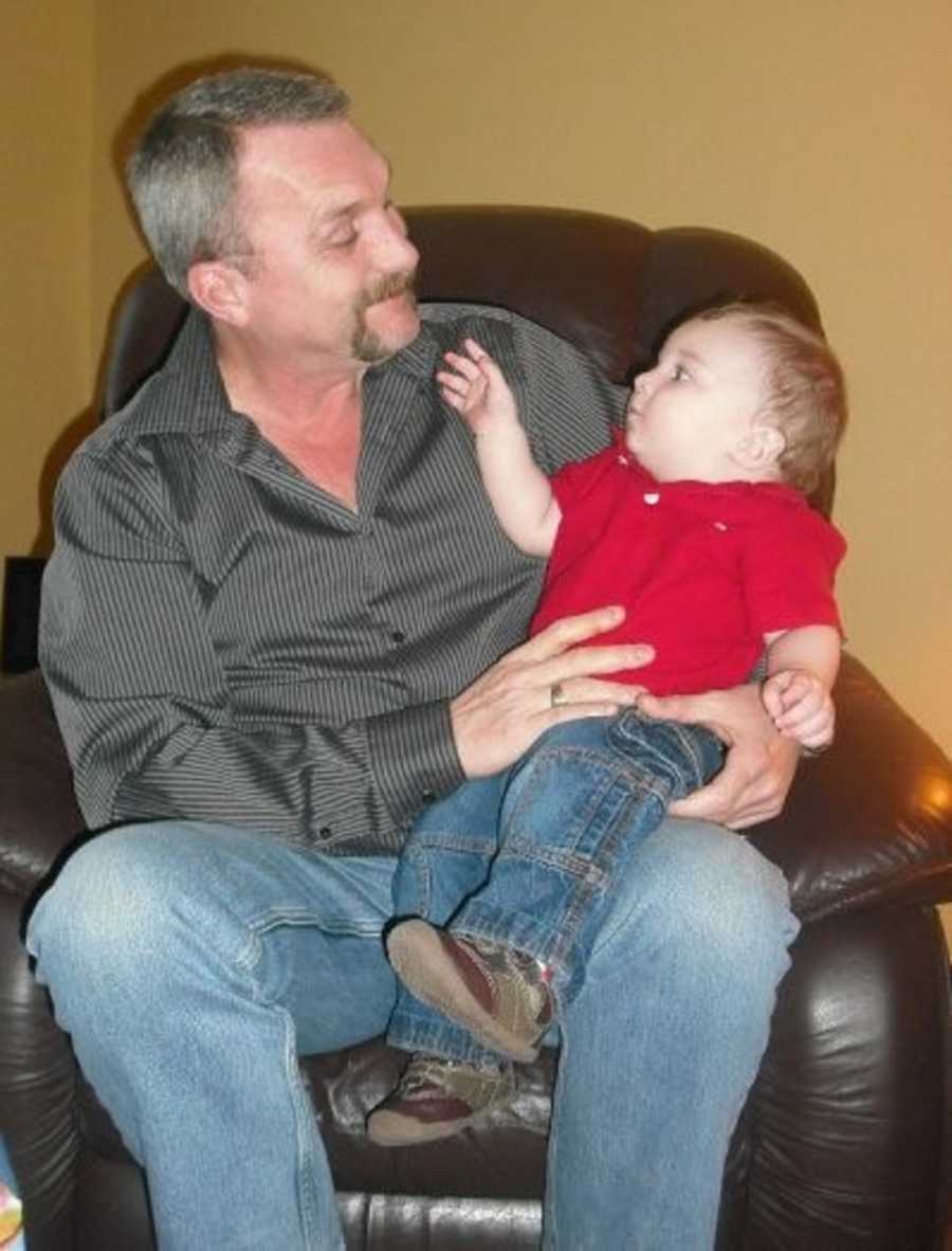 Man sits in leather chair in home smiling at grandson sitting in his lap