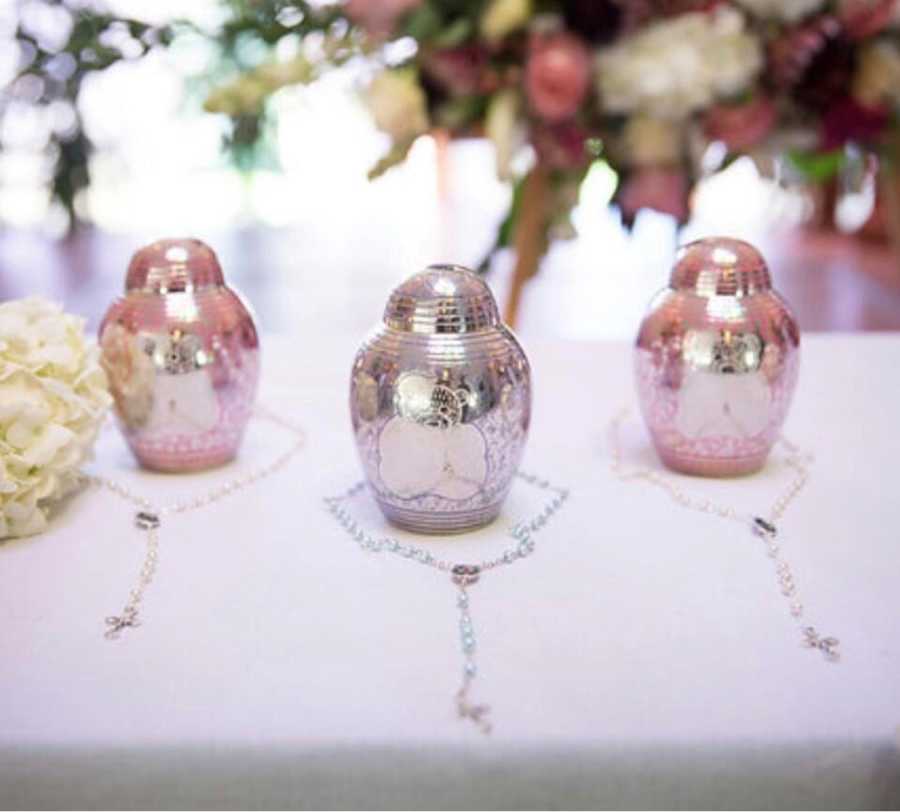 Three urns sit on table with necklaces around them for wives lost children
