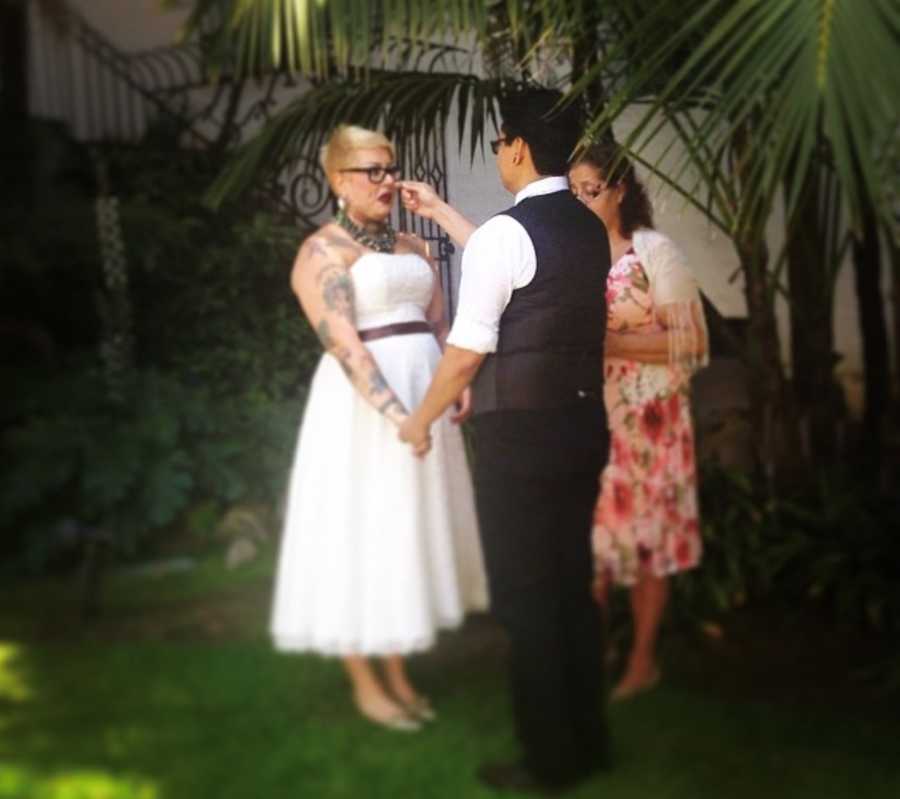 Wife and wife stand outside with officiant at wedding