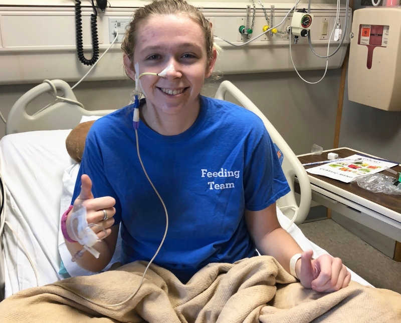 Young woman with Elher's Danlos Syndrome sits in hospital bed with thumbs up