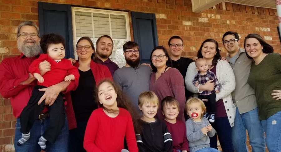 Husband and wife stand outside home with their two foster children and four biological kids and their families