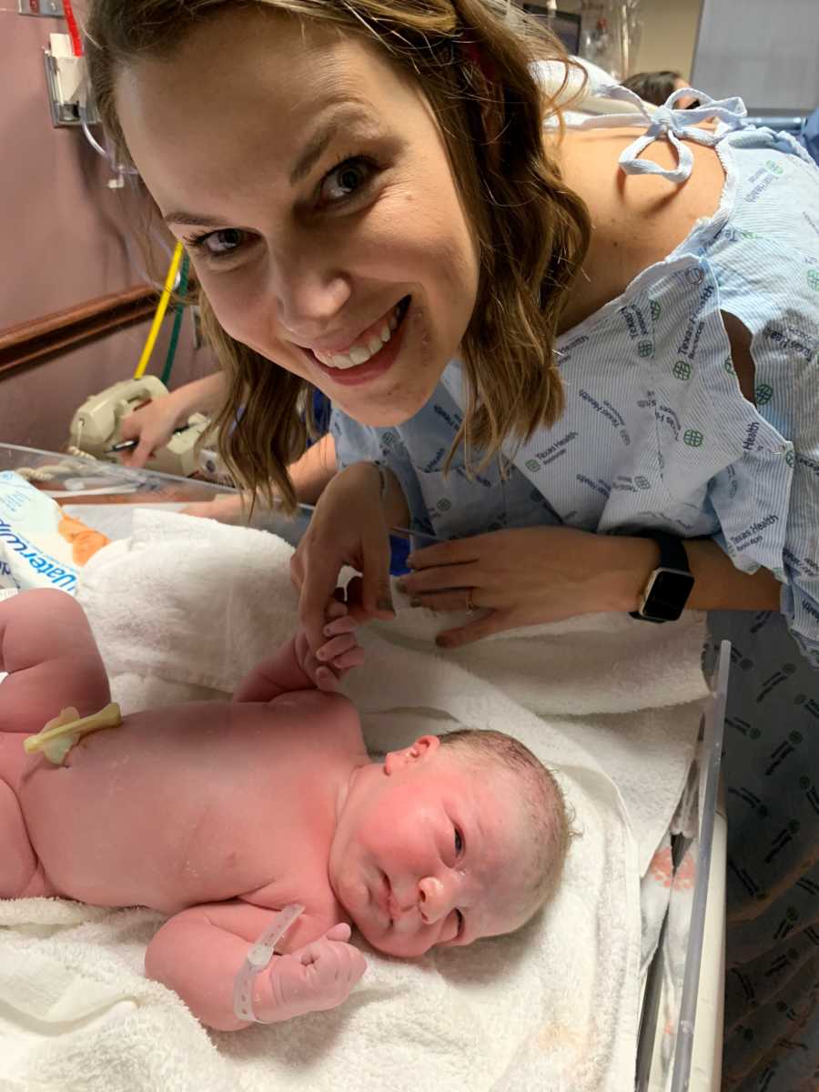 Woman stands smiling above newborn that she is adopting