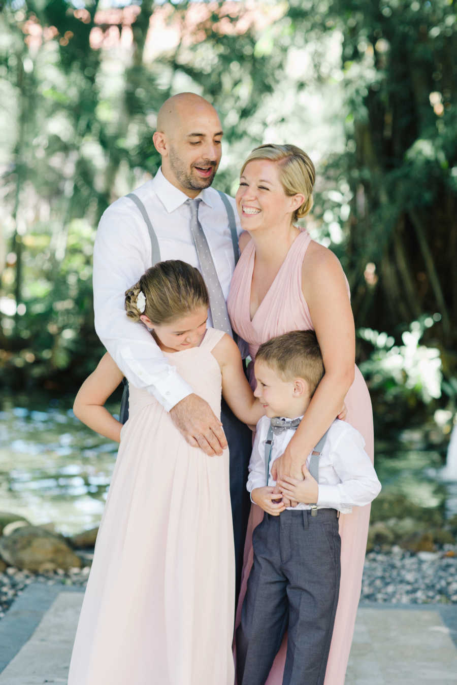 Woman smiles outside with her late husband and two young kids who are all in formal clothing