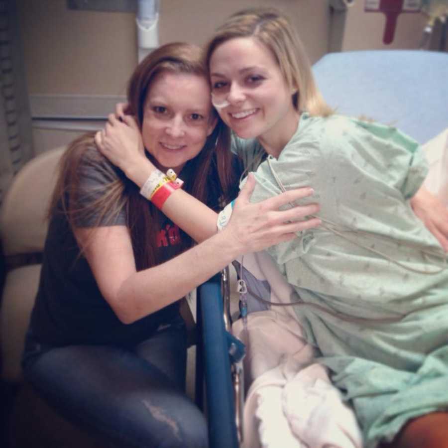 Woman with gastroparesis sits in hospital bed hugging mother who sits in chair beside her