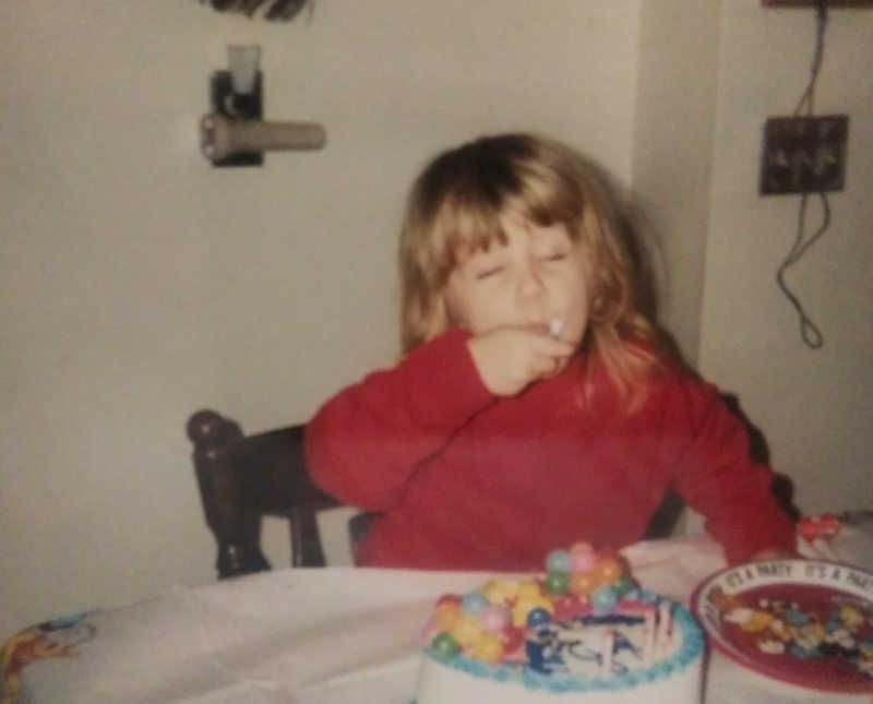 Little girl sits at table in home eating birthday cake